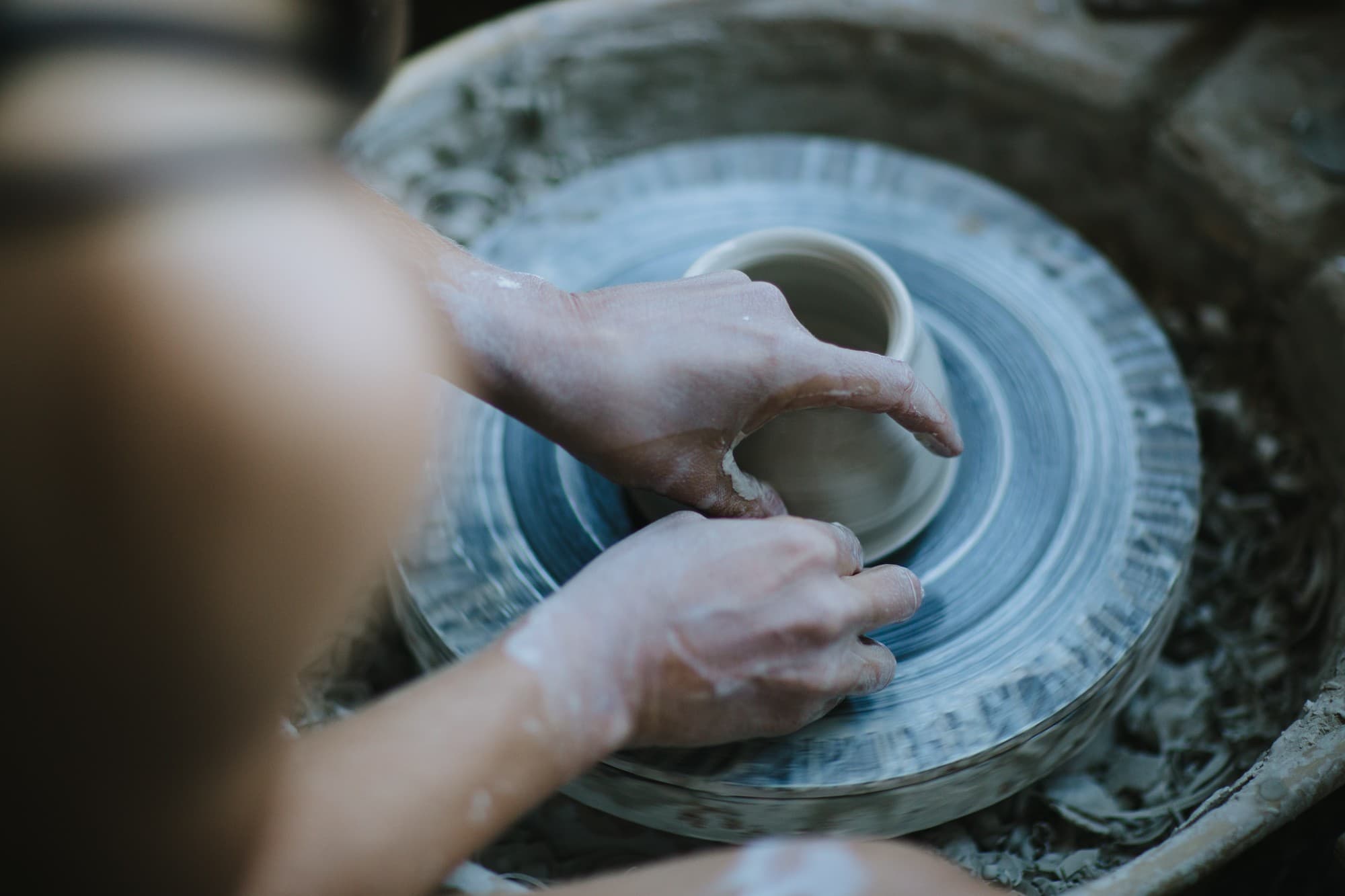 A potter's clay-dusted hands shaping a bowl on the wheel